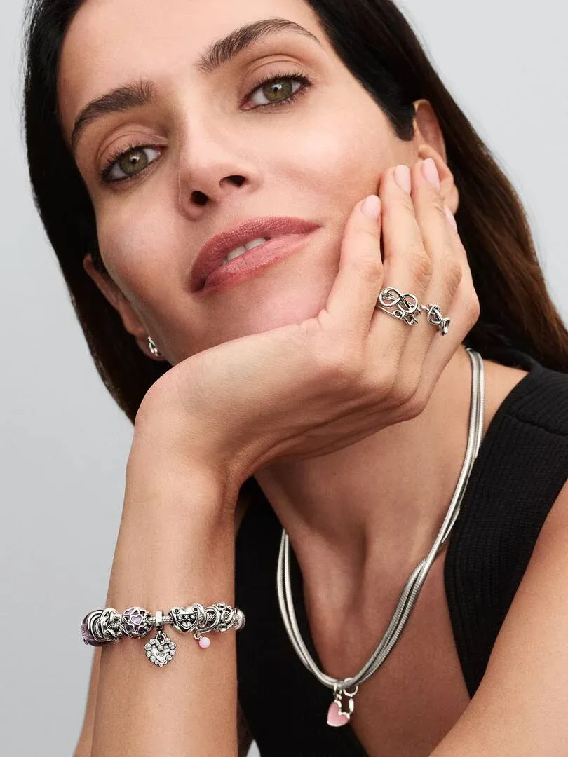 Primer plano de mujer con collar y pulsera de plata, mano apoyada en la cara, fondo neutro.