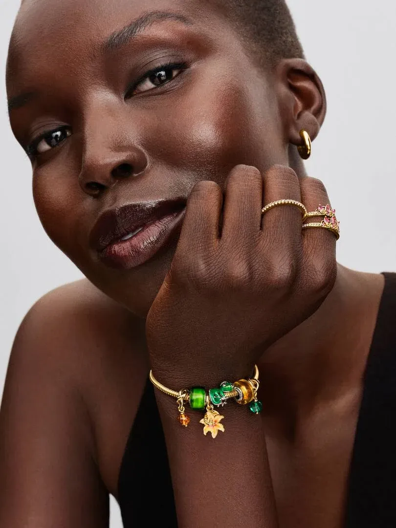 Primer plano de mano con pulsera y anillos, modelo apoyada en la barbilla sobre fondo gris neutro.