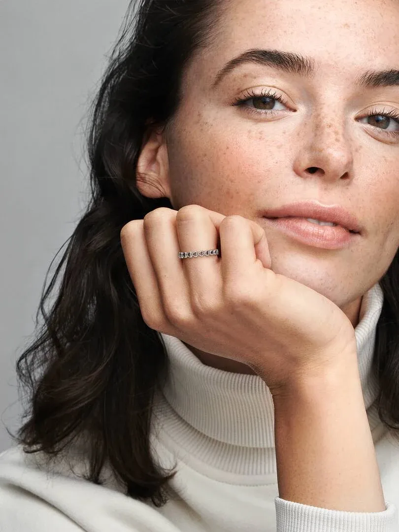 Nahaufnahme des Herzrings am Ringfinger, Modell stützt das Kinn auf ihre Hand.