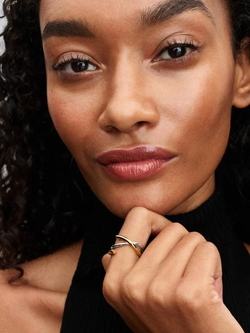 Primer plano de anillo bicolor en dedo, modelo apoyando la barbilla sobre su mano.