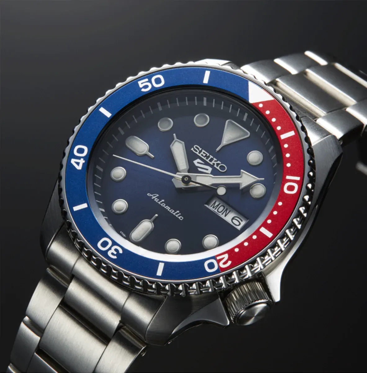 Toma en perspectiva del dial azul y bisel bicolor rojo y azul, fondo neutro oscuro.