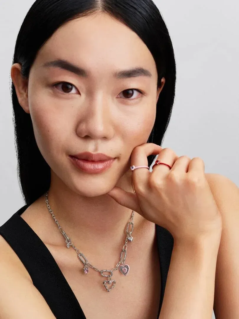 Gros plan d'un modèle portant un collier à maillons et des bagues, vue de face sur fond neutre.