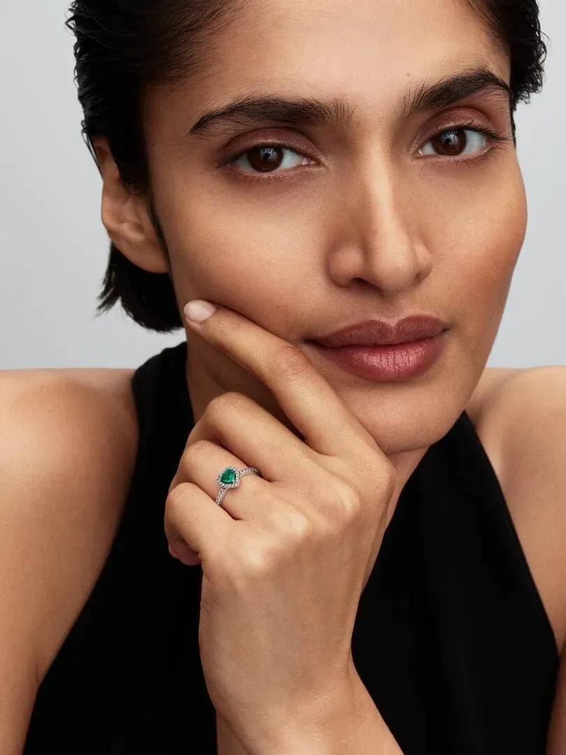 Close-up of a hand resting on the chin, showcasing the green stone ring on the ring finger.