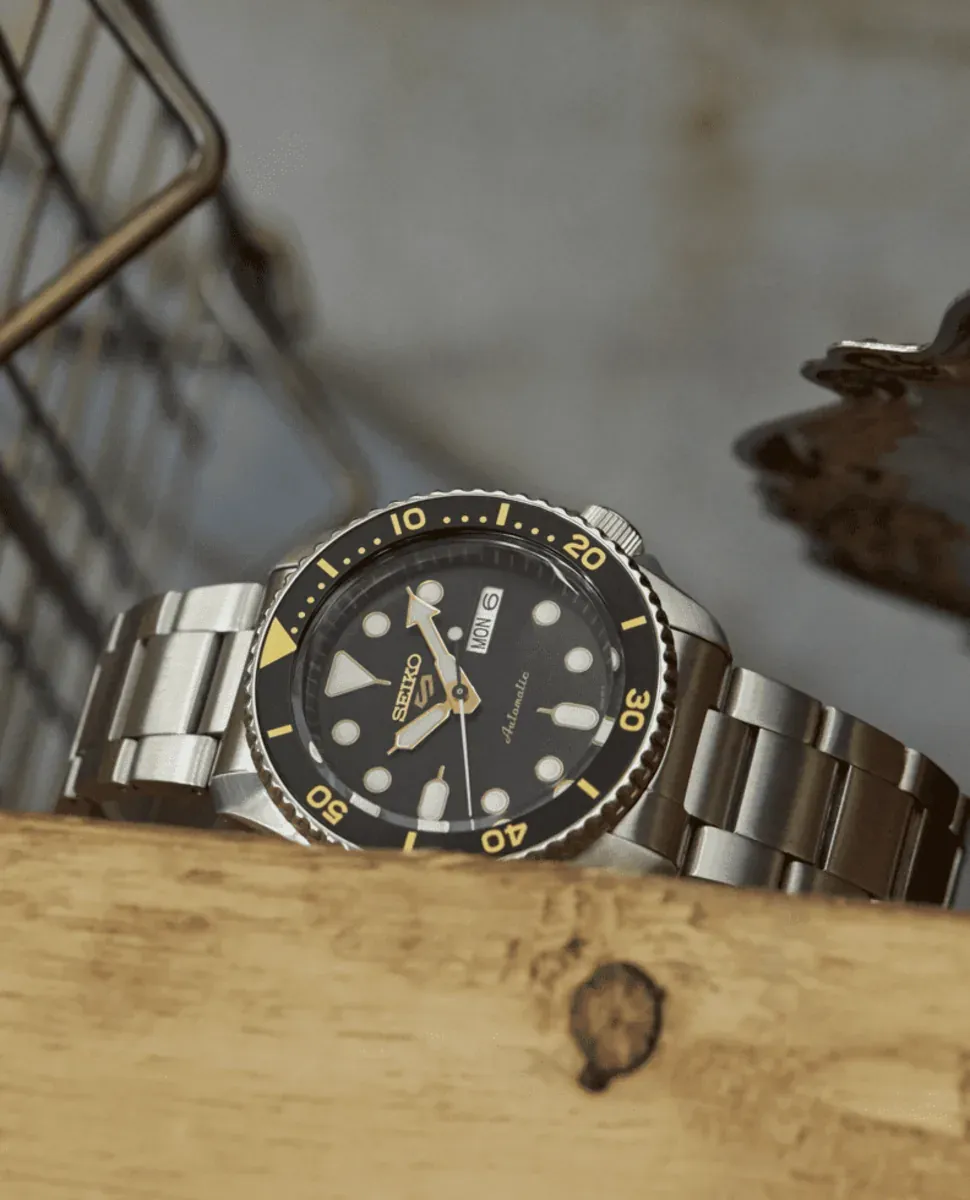 Reloj apoyado sobre superficie de madera, vista en ángulo con fondo neutro desenfocado.