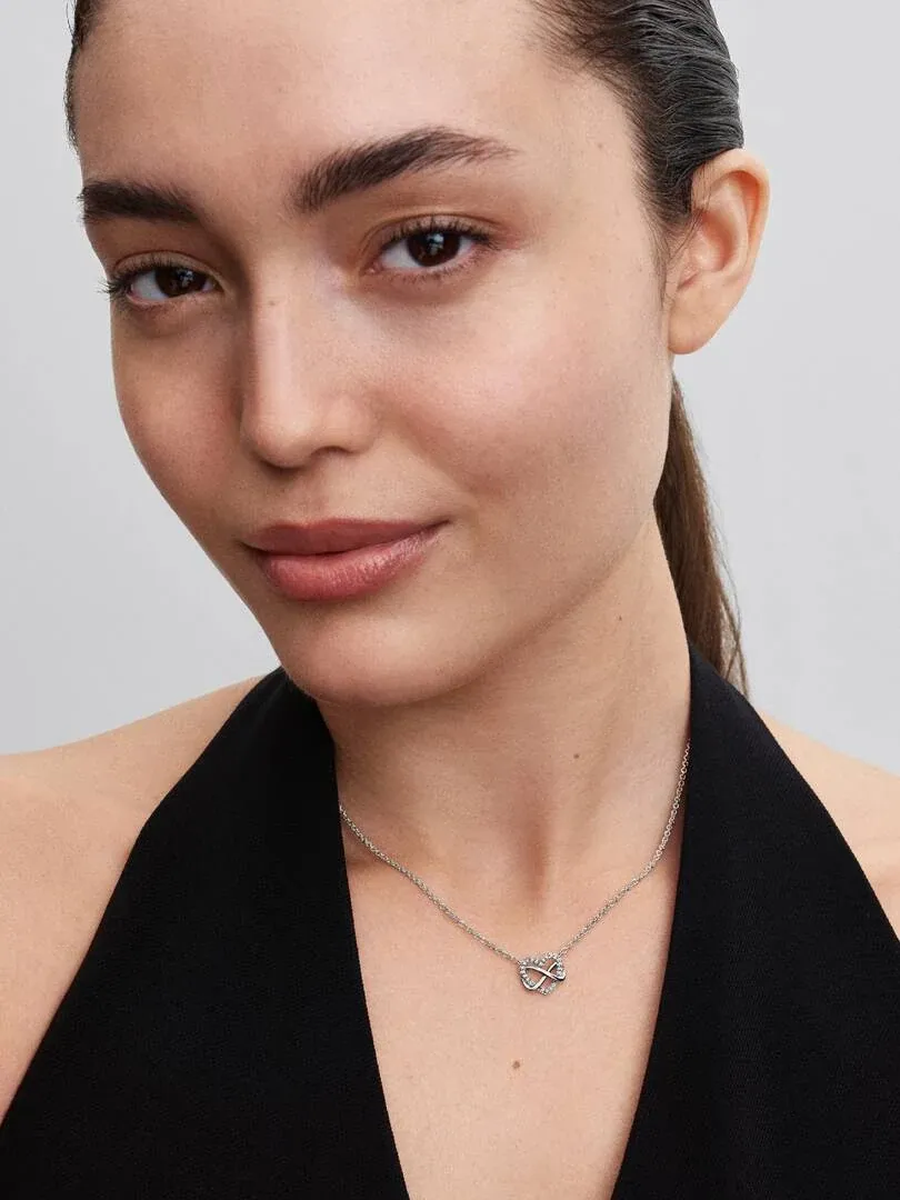 Nahaufnahme des Herzanhängers am Hals eines Models, mit schwarzem Oberteil vor neutralem Hintergrund.