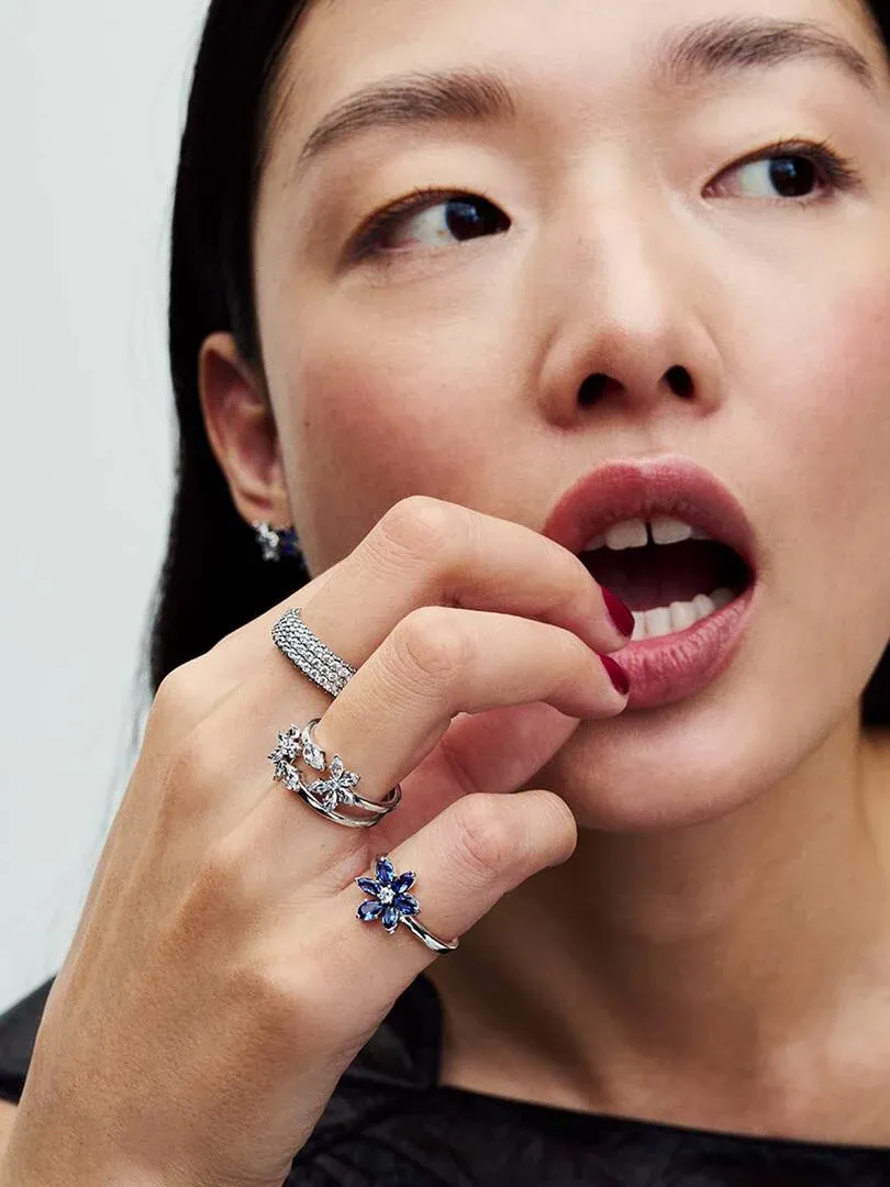 Close-up of hand wearing floral rings, side view near face, neutral background.