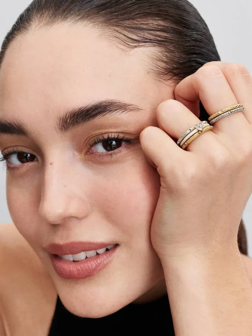 Primer plano de mano femenina con dos anillos apilados, toma lateral cerca del rostro.