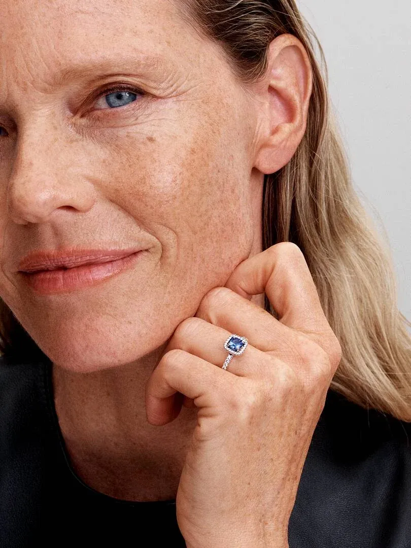 Close-up of blue stone ring on ring finger, model posing with hand near face.