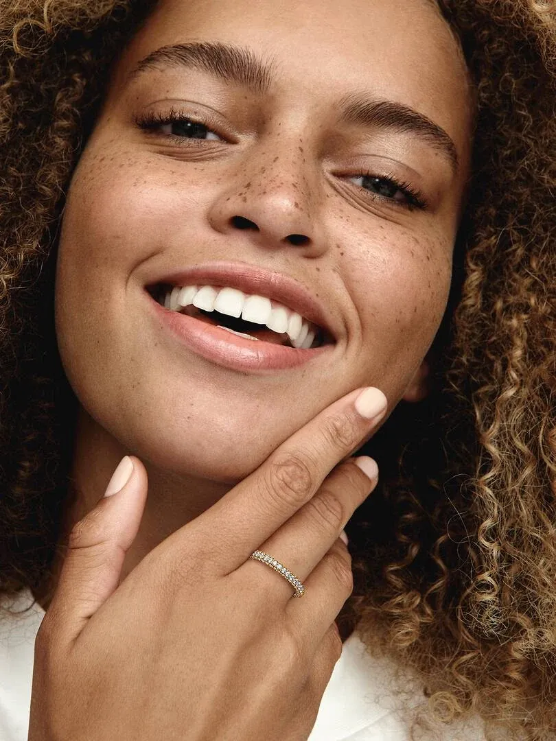 Primer plano de una mujer sonriendo con el anillo pavé en su dedo, toma lateral cerca del rostro.