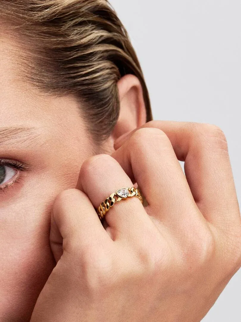 Primer plano del anillo de cadena cubana con circonita en forma de corazón, puesto en el dedo, fondo neutro.