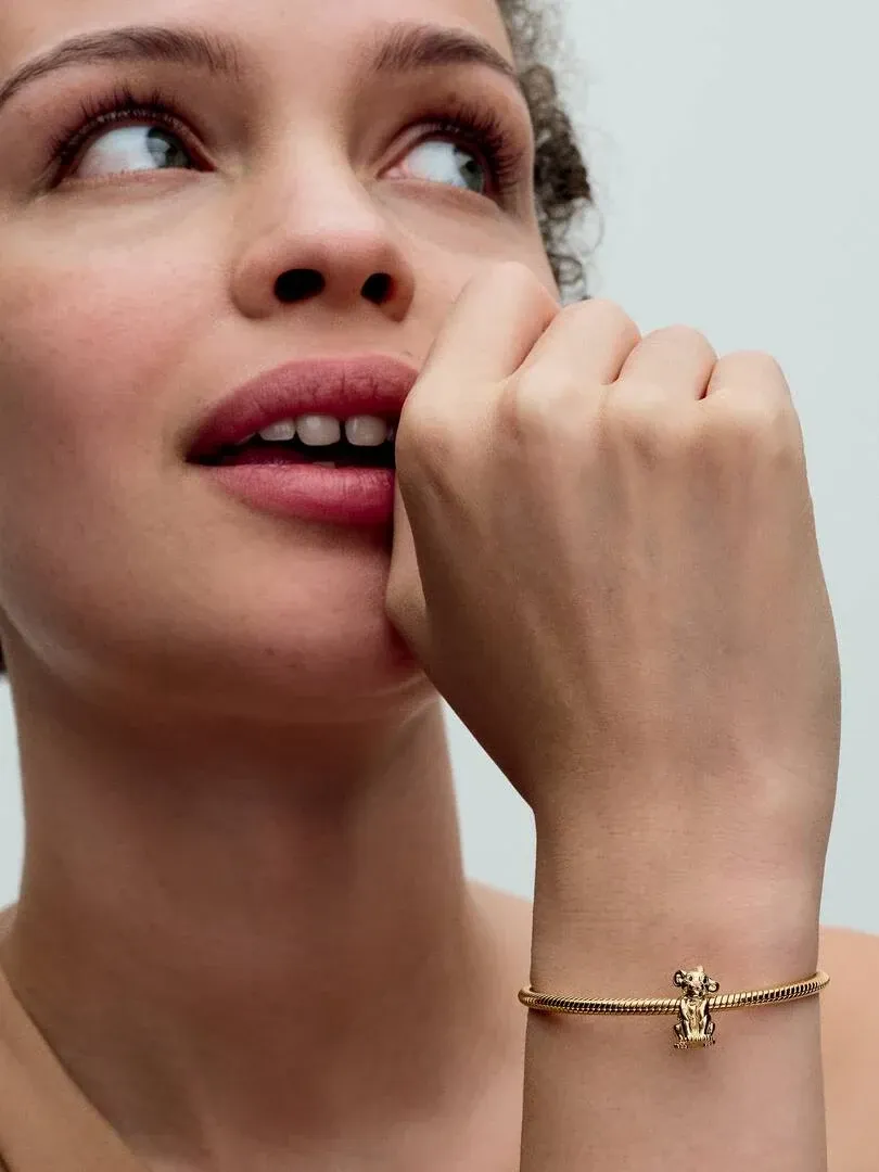 Gros plan du poignet avec le charm Simba sur un bracelet doré, vue de profil sur fond neutre.