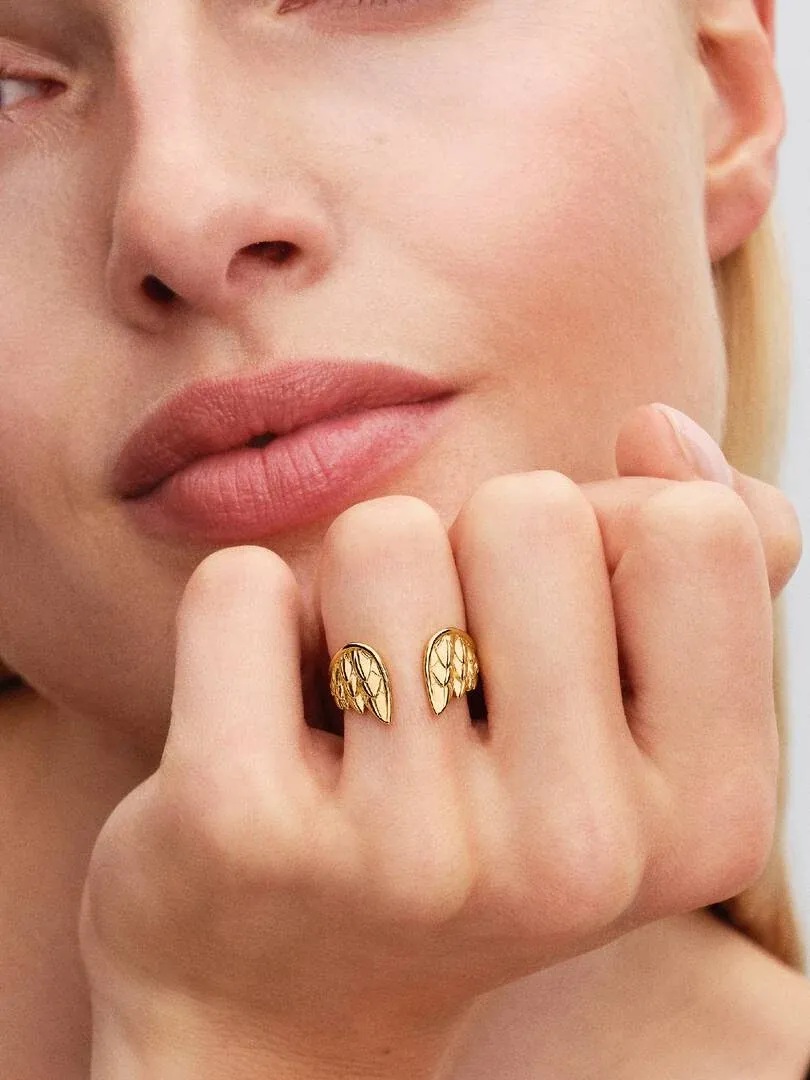 Primer plano del anillo abierto con detalles de alas en el dedo, toma lateral sobre mano de modelo.