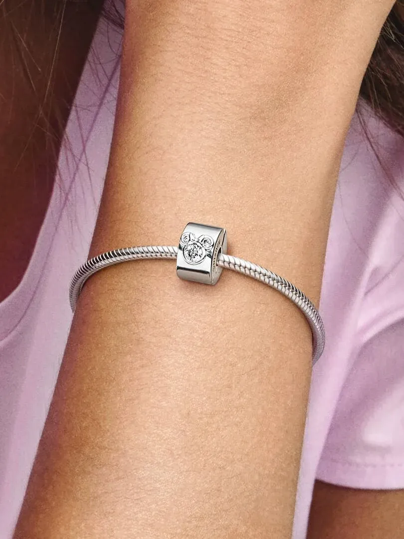 Primer plano del clip de Mickey y Minnie en una pulsera de plata, sobre la muñeca con fondo rosa suave.