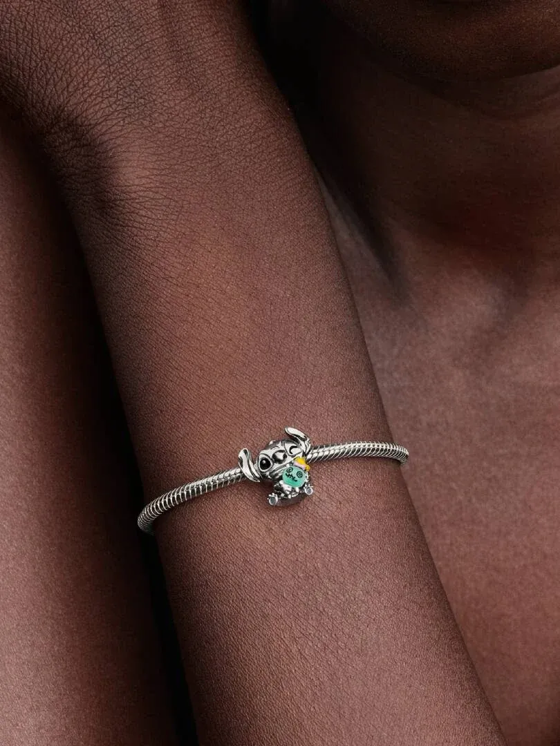Primer plano del charm de Stitch en una pulsera de plata, puesto en la muñeca con fondo desenfocado.