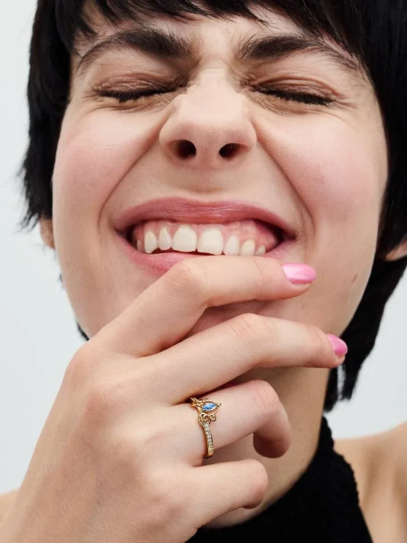 Primer plano de la mano apoyada en el rostro, mostrando el anillo con gema azul en el dedo anular.