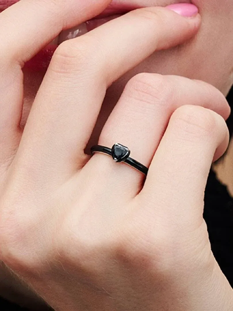 Gros plan de la bague à cœur noir portée sur un doigt, vue de profil sur la peau.