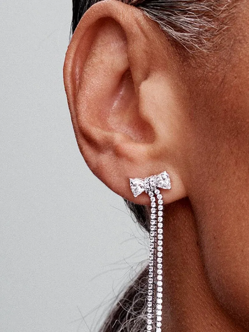 Gros plan latéral d'une boucle d'oreille pendante avec nœud et pavé de zircons portée à l'oreille.