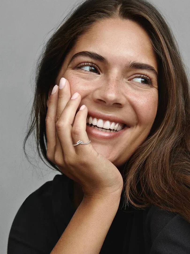 Primer plano de una mujer sonriendo con el anillo de tiara en el dedo, toma lateral sobre fondo neutro.