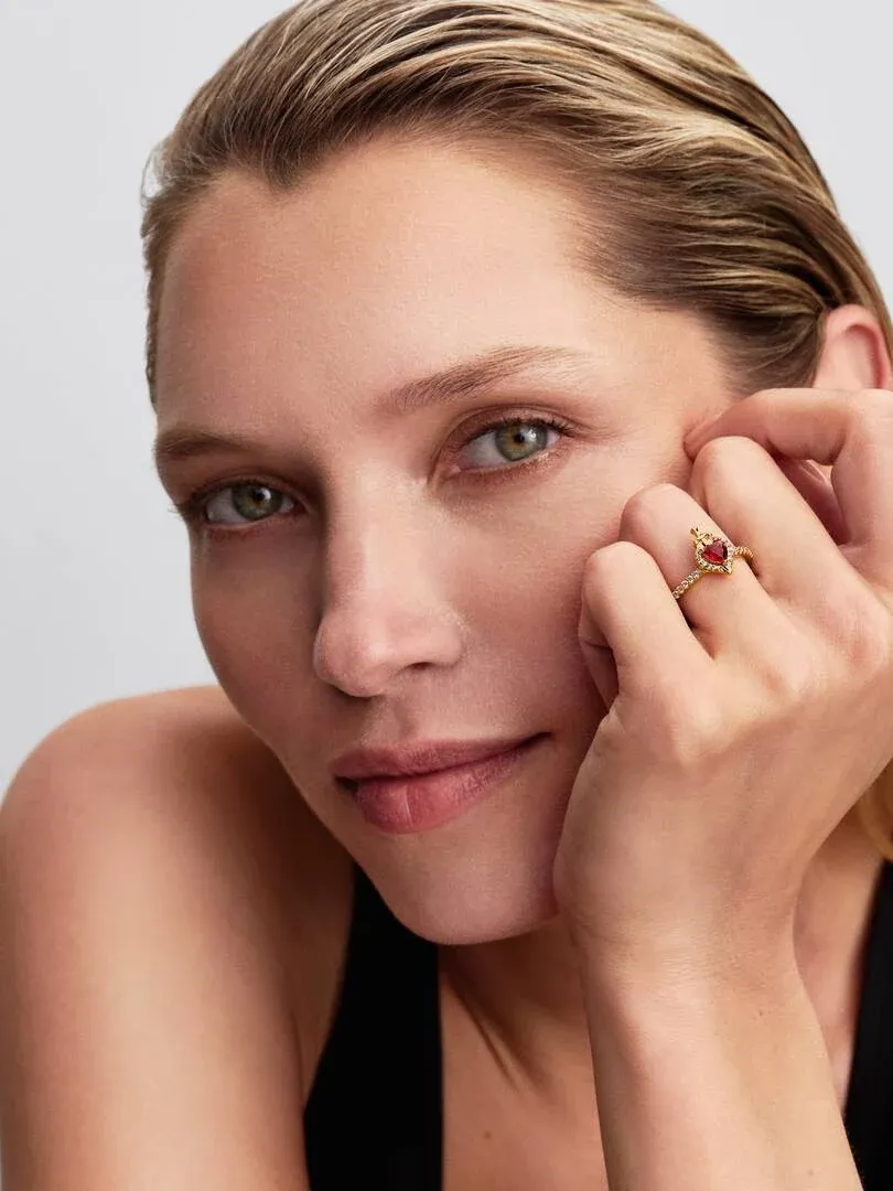 Primer plano de anillo con cristal rojo en forma de corazón puesto en el dedo, toma lateral sobre mano de modelo.