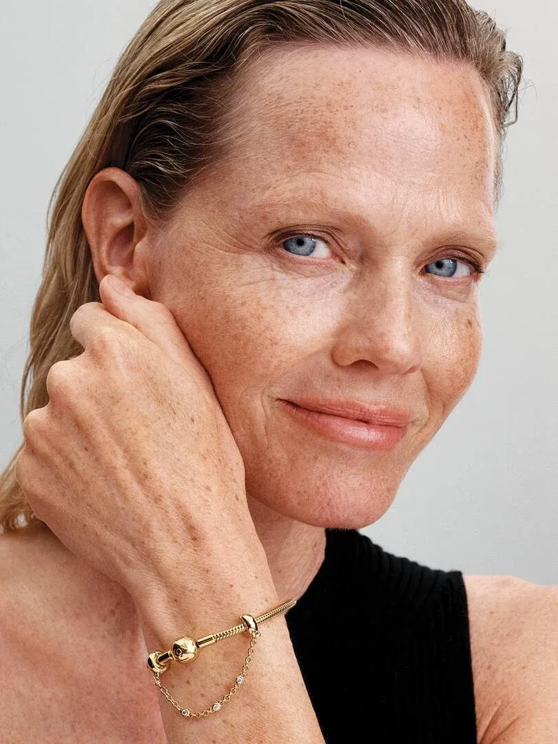 Gros plan d'une chaîne de sécurité dorée avec gemmes sur un poignet, posé contre le visage d'un modèle.