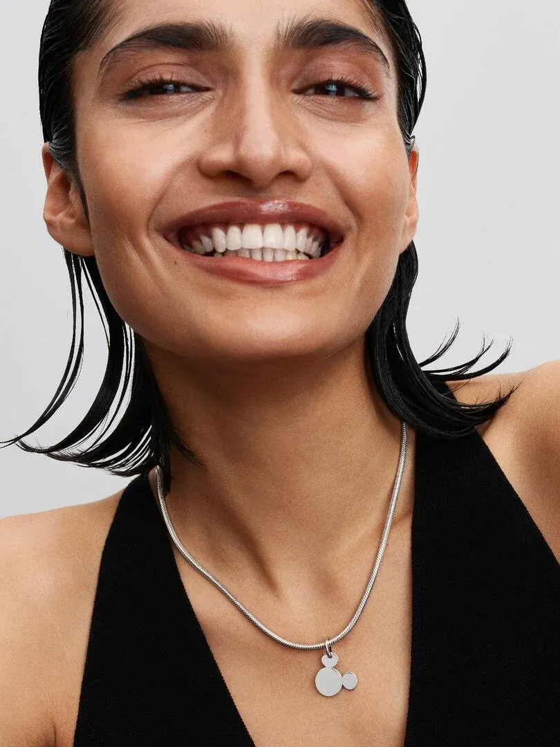 Primer plano de collar con colgante de Mickey Mouse sobre cuello y escote, fondo neutro.