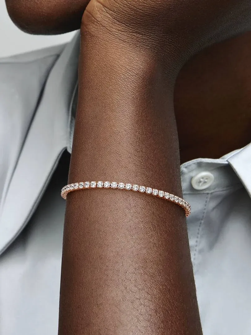 Primer plano de la pulsera de tenis sobre una muñeca, toma lateral con camisa blanca de fondo.