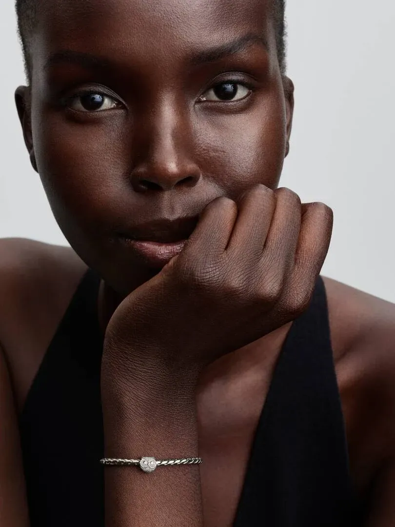 Close-up of the owl charm on a bracelet worn by a model resting her chin on her hand.