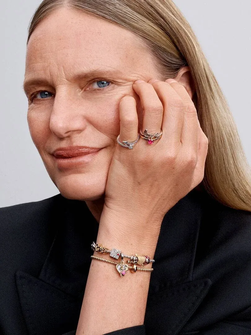 Primer plano de mano con anillo y pulsera, modelo apoyando la cara sobre el puño, fondo neutro.