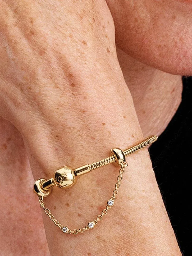 Gros plan de la chaîne de sécurité dorée avec gemmes sur un poignet, vue latérale en angle diagonal.