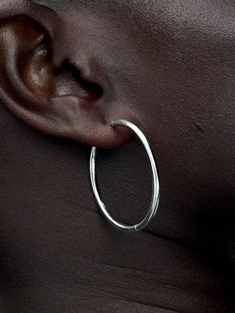 Gros plan latéral d'une boucle d'oreille créole en argent portée à l'oreille sur peau foncée.
