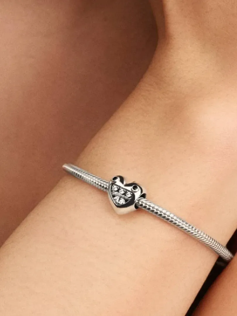 Primer plano de charm de corazón en pulsera de plata, sobre la muñeca con fondo desenfocado.