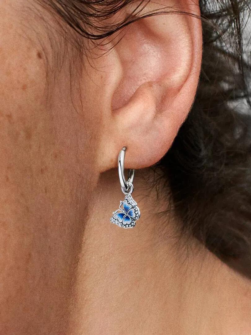 Primer plano lateral de pendiente de aro con colgante de mariposa azul puesto en la oreja.