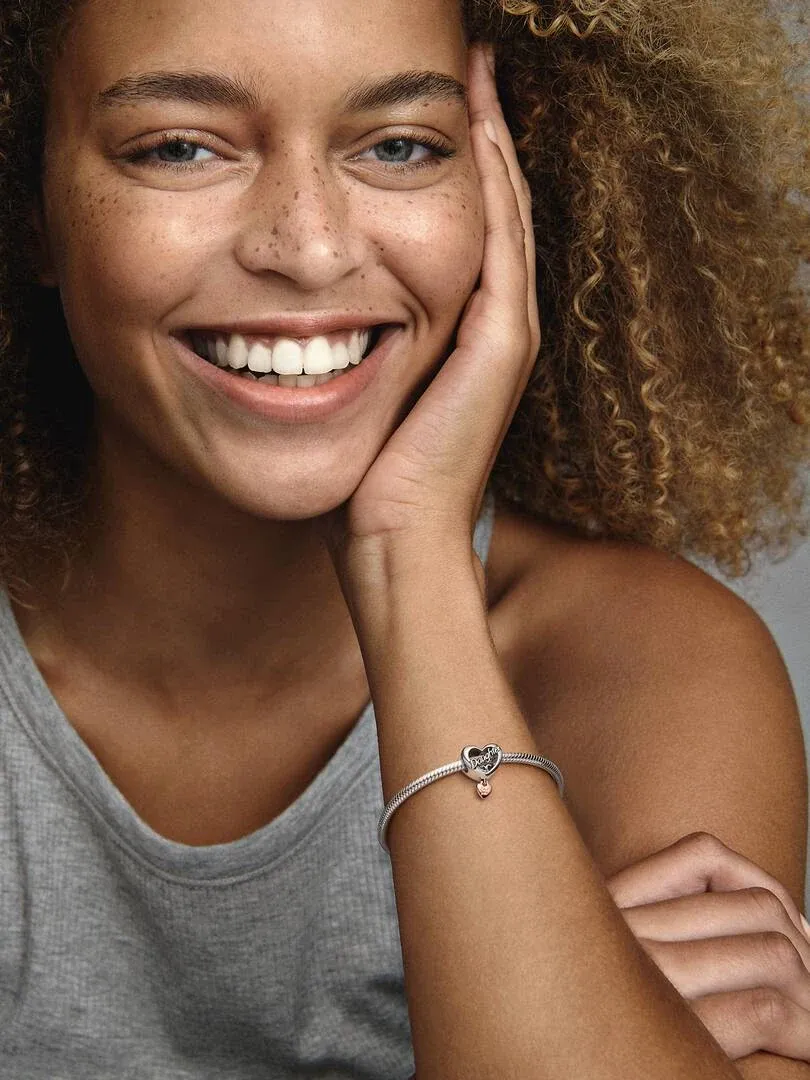 Close-up of a smiling woman wearing the heart charm on her bracelet, side view at chest level.