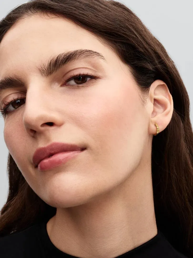 Gros plan latéral d'une boucle d'oreille huggie dorée avec cristaux jaunes portée sur le lobe de l'oreille.