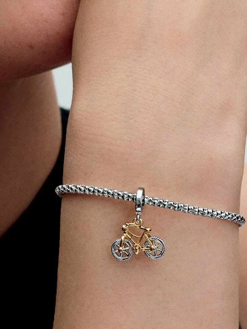 Twee kleuren fiets charm hangend aan een zilveren armband, zijaanzicht op een pols.