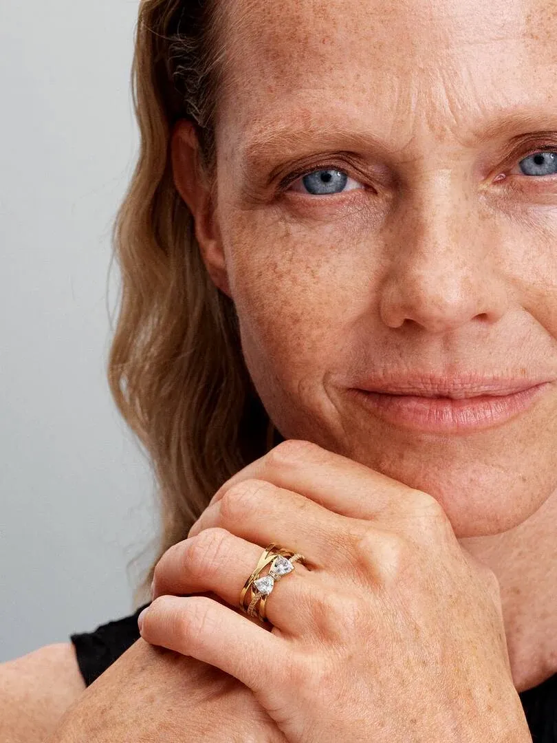 Primer plano del anillo de bandas cruzadas en el dedo anular, mano apoyada bajo la barbilla.