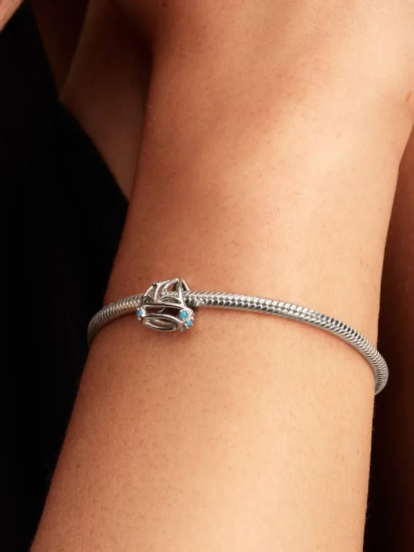 Primer plano del charm de velero en una pulsera de plata sobre la muñeca, toma lateral con fondo oscuro.