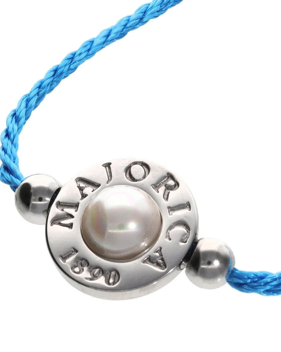 Close-up of the half-sphere pearl and engraved metal charm on blue braided cord, white background.