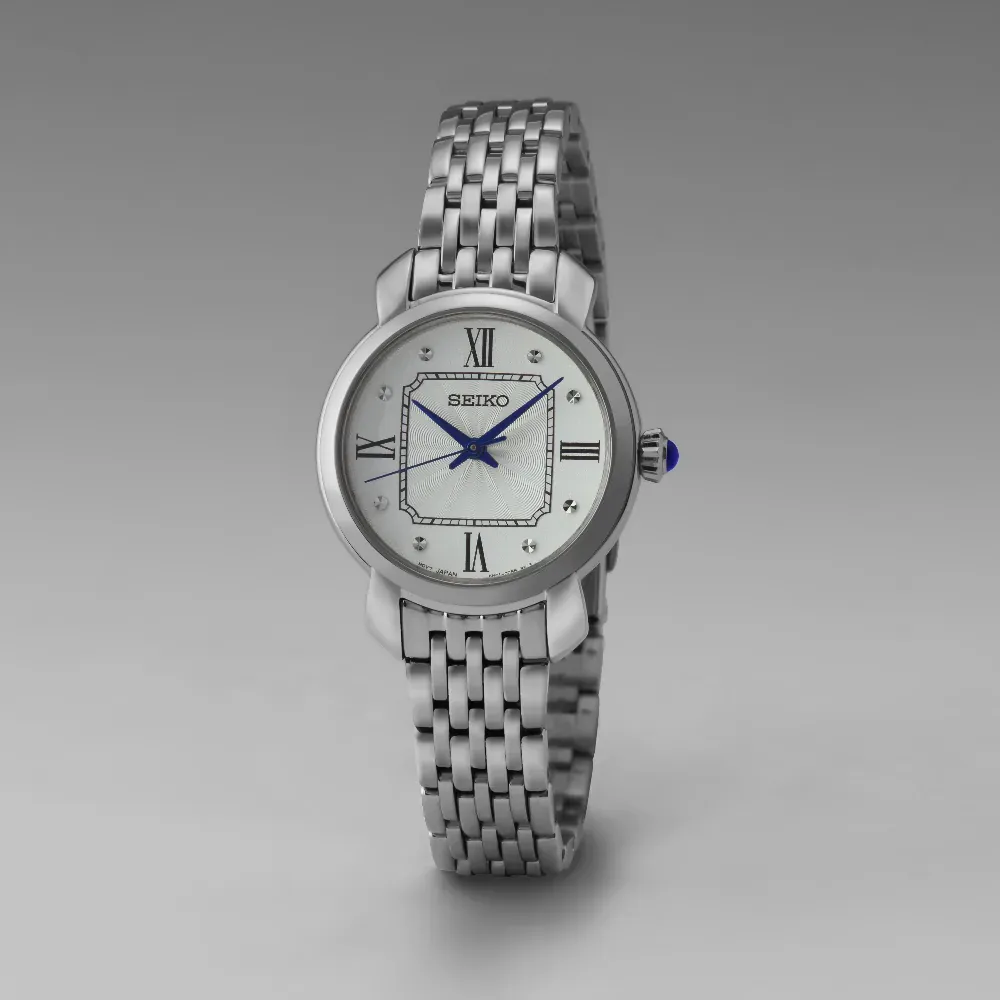 Vista frontal del reloj centrado sobre fondo gris neutro, mostrando la esfera y el brazalete.