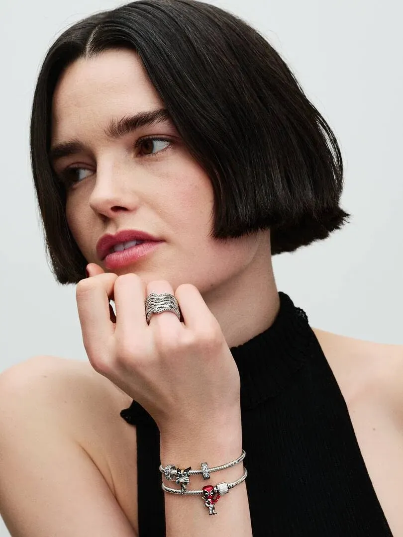 Gros plan d'une main portant un bracelet en argent avec charm rouge, modèle en haut noir sur fond neutre.