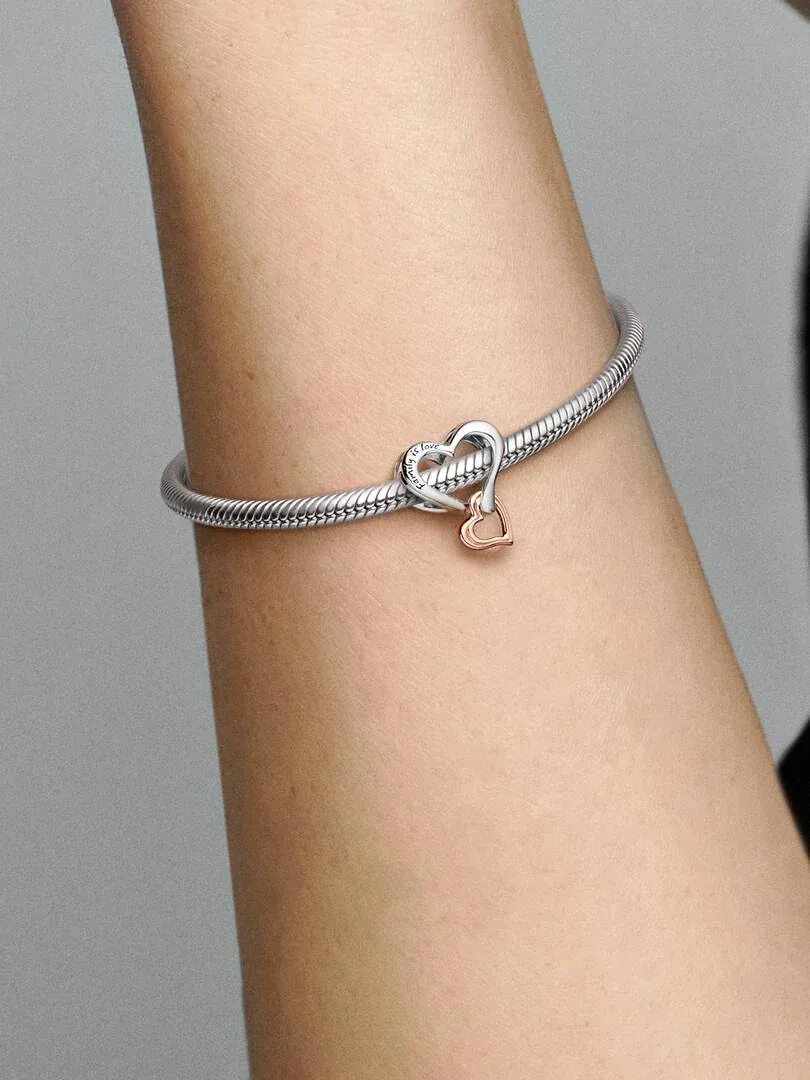 Primer plano del charm de corazones en una pulsera de plata, puesto en la muñeca sobre fondo gris neutro.