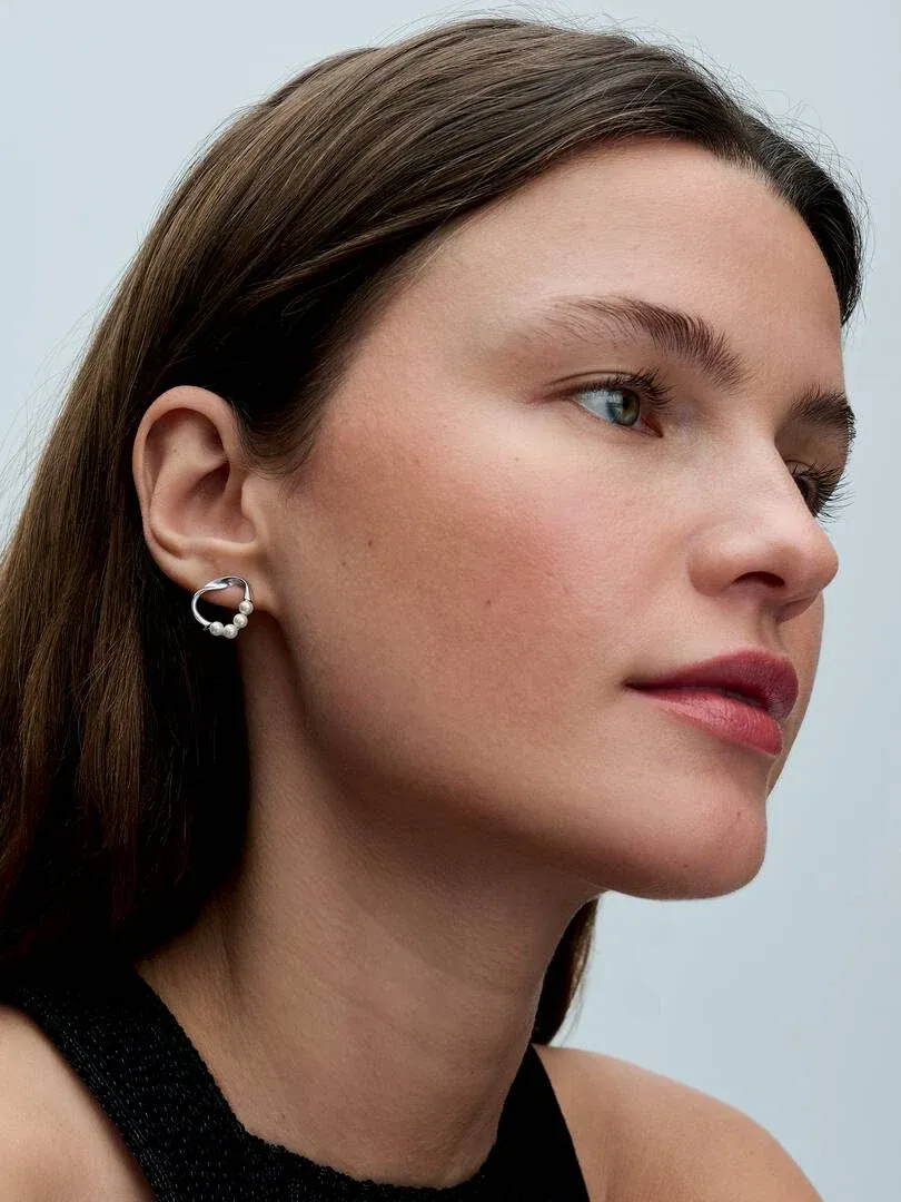 Gros plan de profil d'un modèle portant la boucle d'oreille en perles, fond neutre clair.