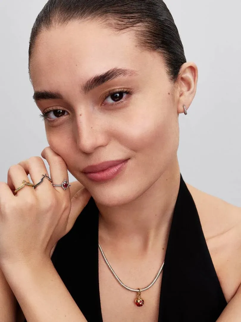 Modelo con collar y anillos, primer plano de rostro y mano apoyada en la mejilla, fondo neutro claro.