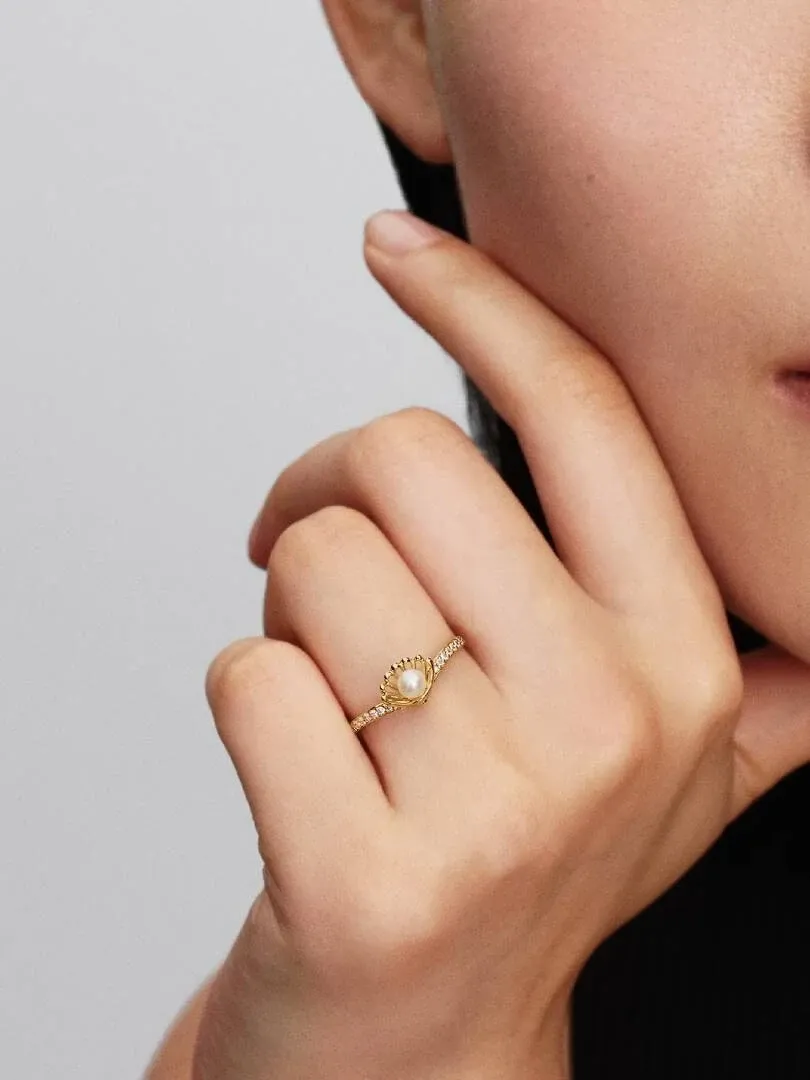 Primer plano del anillo de concha y perla en el dedo anular, toma lateral sobre mano con fondo neutro.