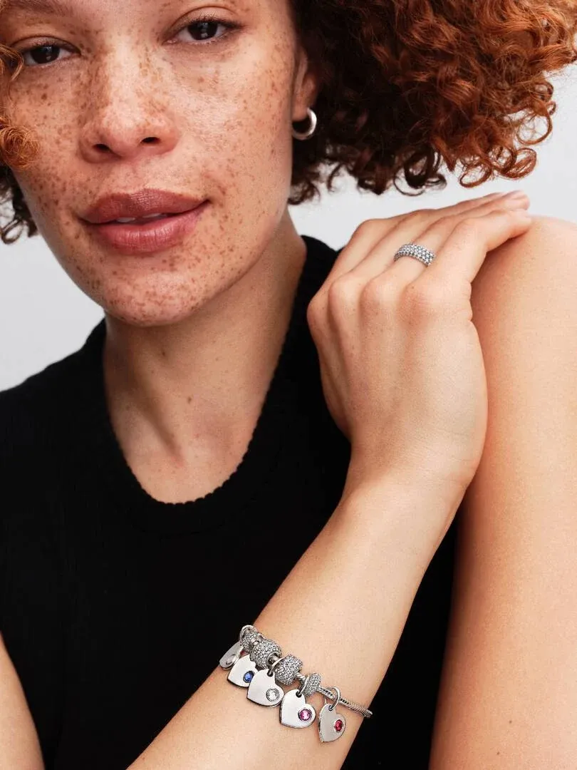 Close-up van hartvormige charm armband om de pols, zijaanzicht met model en wazige achtergrond.