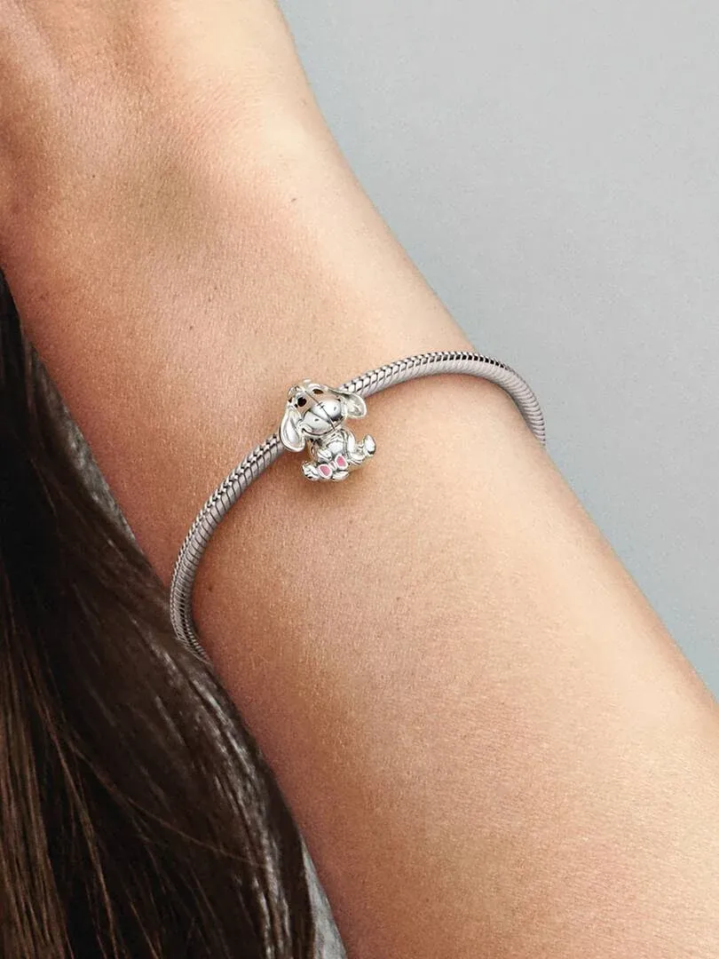 Primer plano de charm de plata con personaje sentado en una pulsera de eslabones, sobre la muñeca.