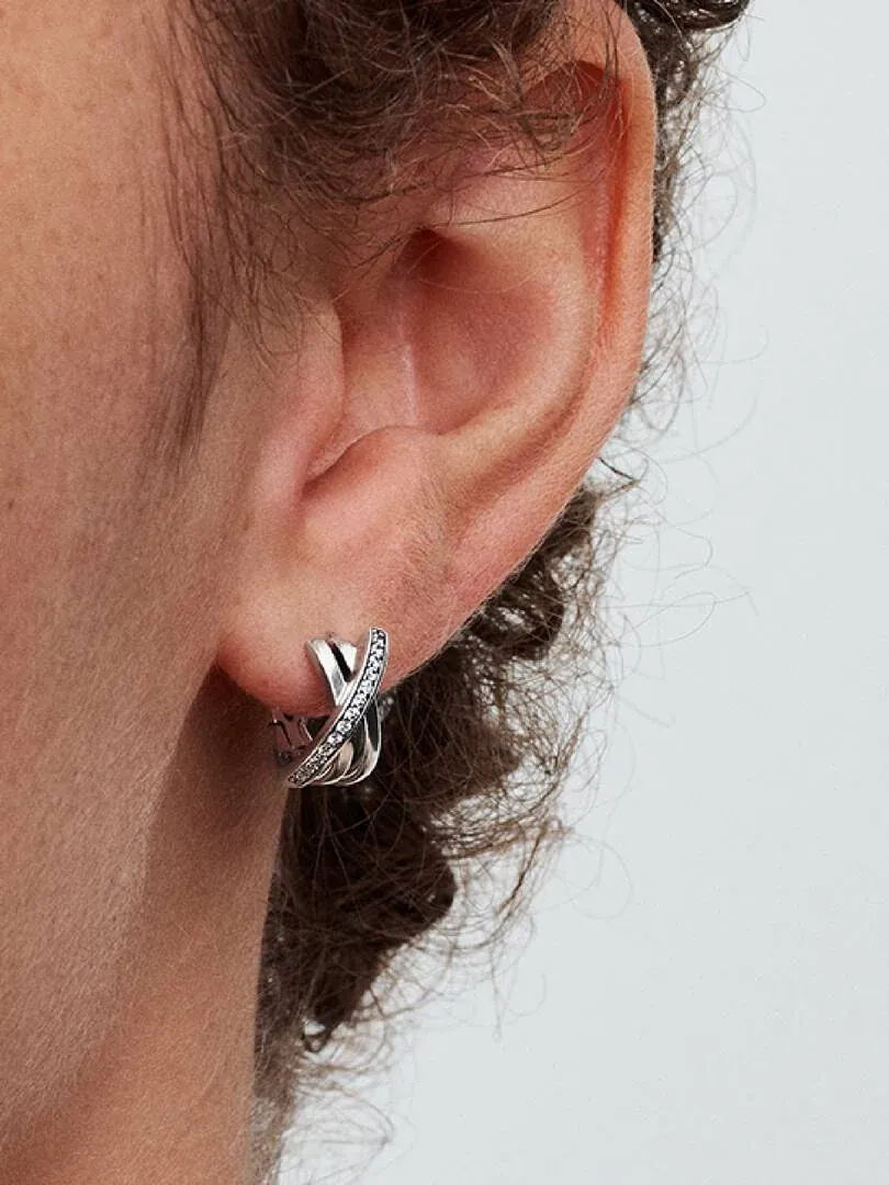 Primer plano lateral de pendiente de aro cruzado con circonitas puesto en la oreja, fondo neutro.