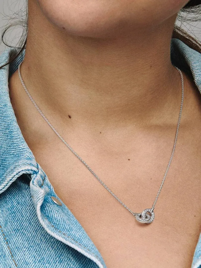Gros plan du pendentif à cercles entrelacés avec zircons sur un cou et des vêtements en jean.