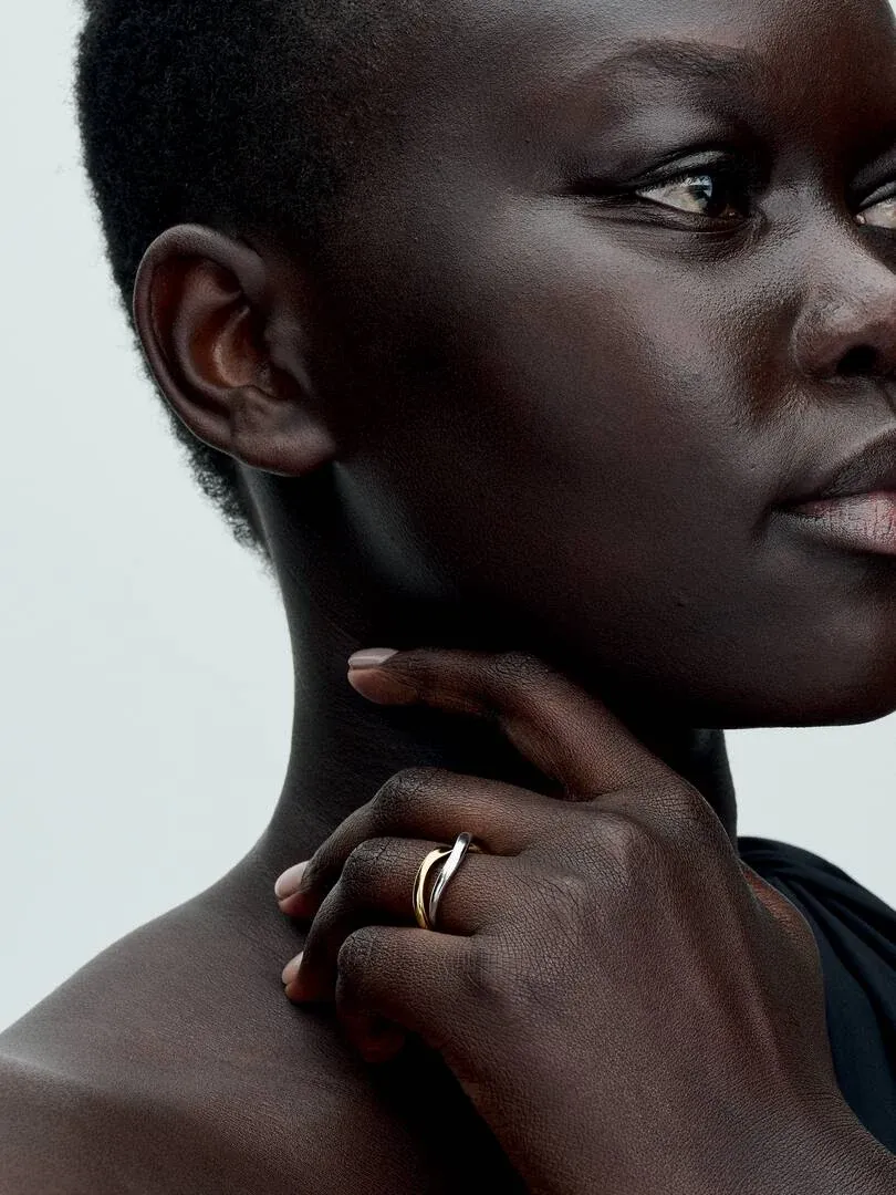 Primer plano del anillo de bandas entrelazadas en el dedo, toma lateral sobre piel, fondo neutro claro.