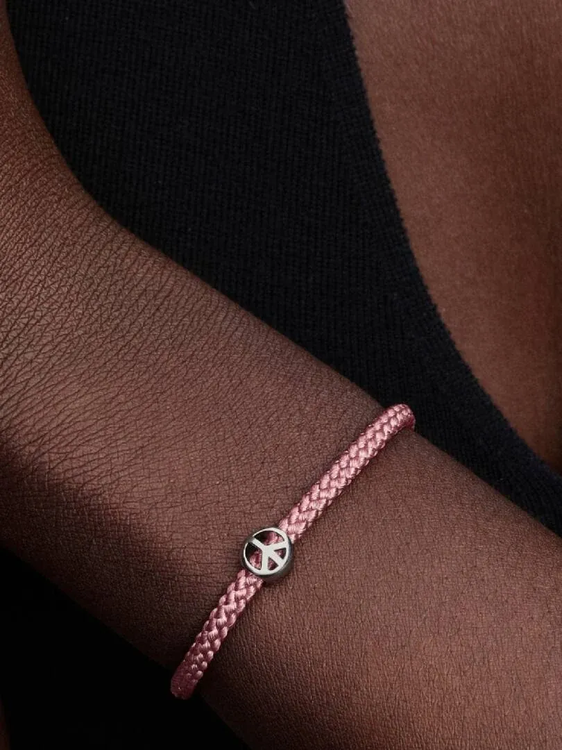 Primer plano de la pulsera rosa con charm de símbolo de la paz en la muñeca, ángulo lateral sobre fondo oscuro.